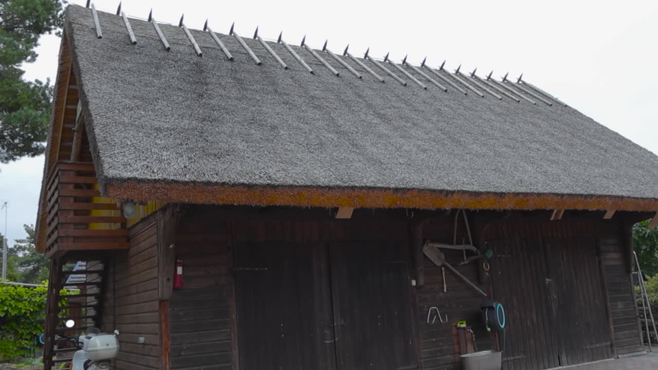 Old traditional wooden house or a building in Saaremaa that has a straw or a rye roof with a balcony during summer time. surrounded by poppy stone roads and some garden equipment is on the sides.