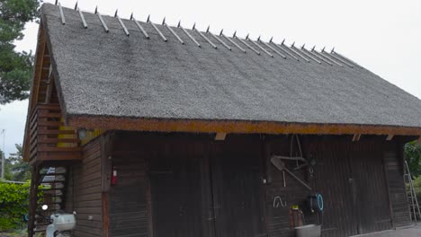 old traditional wooden house or a building in saaremaa that has a straw or a rye roof with a balcony during summer time. surrounded by poppy stone roads and some garden equipment is on the sides.
