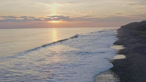 amazing sunset over beach shoreline, waves crashing against pebble beach, aerial