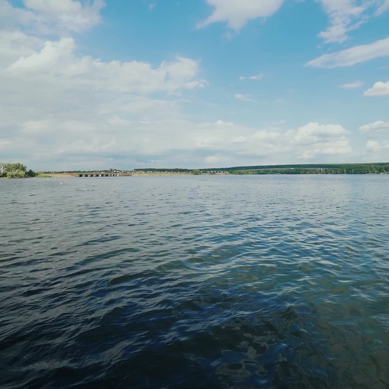 View from the side deck of the yacht. Motor boat moves along the shore, creating waves.