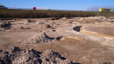Panning view across archaeology site, traffic drives on highway in background