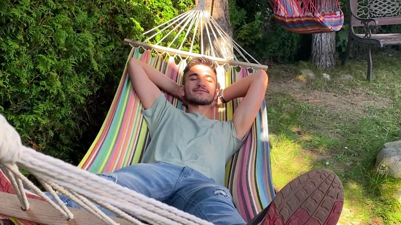 Primo piano di un ragazzo spensierato e felice che si rilassa su un'amaca colorata in un giardino esterno in vacanza in una giornata di sole