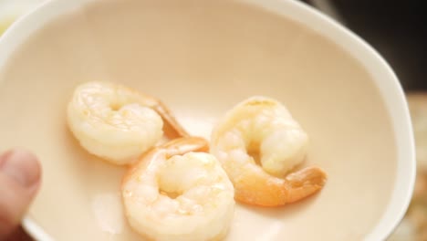unrecognizable person putting fried prawns from pan into bowl