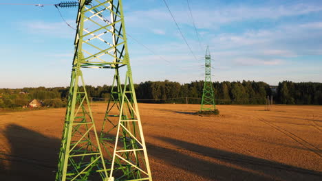 High-voltage-power-line-pole-surrounded-by-agriculture-field,-aerial-ascend-view