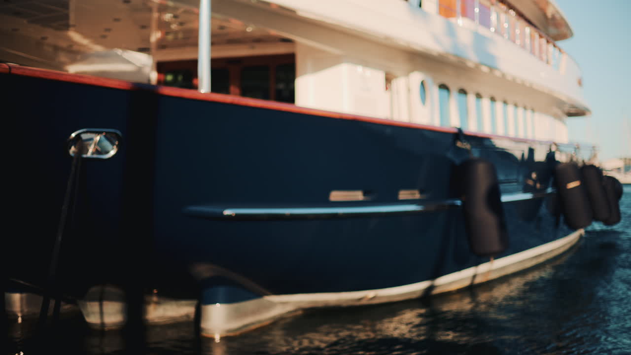 Seitenansicht einer dunkelblauen Luxusyacht mit Chromdetails und Holzdeck, die in einem Jachthafen unter hellem Sonnenlicht schwimmt