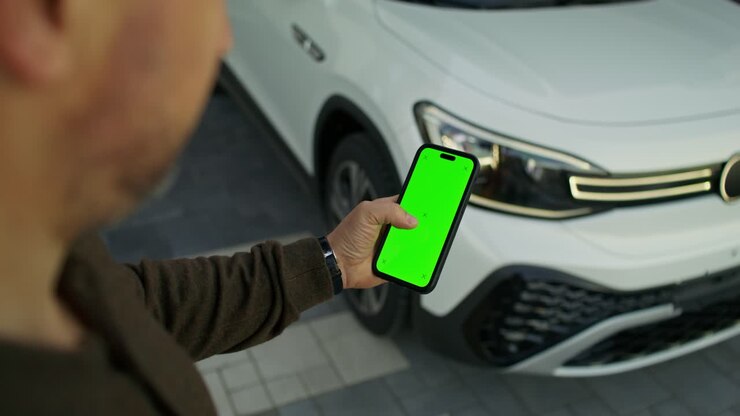 Person holding smartphone with green screen in front of a white SUV