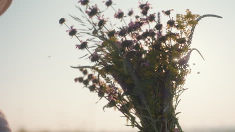 close up of wildflower bouquet held in hand turning slowly against bright sky as sunlight filters through vibrant yellow purple and green petals creating radiant peaceful natural moment