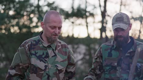 conversation of soldiers in camouflage clothes, they are discussing in the evening by the common bonfire frying sausages for supper, men are resting after work, service, field exercises