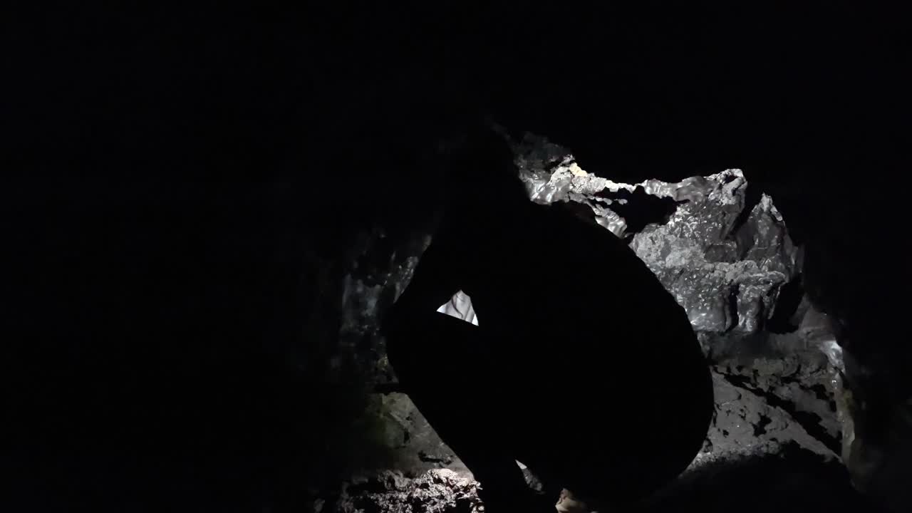 exploradora agazapada en la oscura cueva de lava kaumana, caverna iluminada con antorcha de cabeza