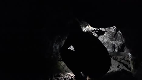 female explorer crouching in dark kaumana lava cave, lighting cavern with head torch