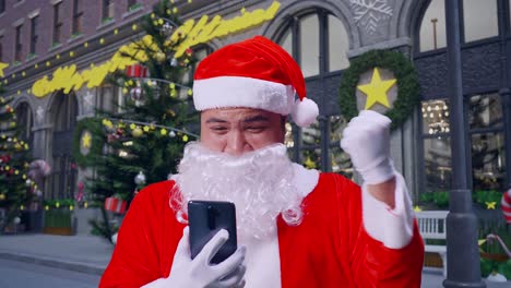 close up of asian santa claus celebrating while using smartphone in christmas night
