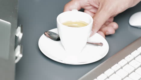 right male hand swiping espresso coffee cup across the table between keyboard mouse and laptop