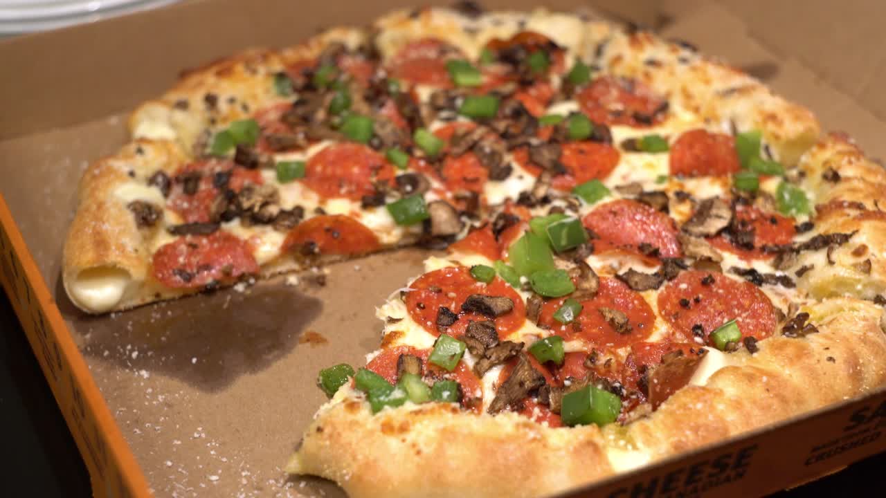 박제 크러스트와 페퍼로니 버섯, 피망을 곁들인 테이크 아웃 배달 피자 상자에서 피자 한 조각을 가져가는 사람의 핸드헬드 샷