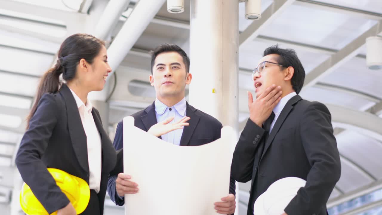 청년 아시아 엔지니어와 사업가들이 블루프린트를 들고 함께 프로젝트를 논의합니다. 프로젝트 관리, 비즈니스 미팅, 전략 및 엔지니어링의 개념.