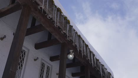 A-mesmerizing-sight-unfolds-as-numerous-glistening-ice-stalactites-delicately-hang-from-the-roof's-edge,-gradually-dissolving-under-the-radiant-rays-of-a-sunny-winter-day