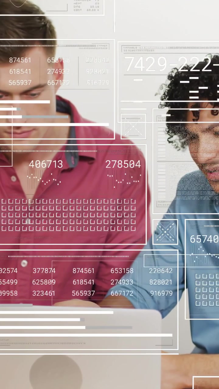 Two male colleagues sitting at desk, tapping laptop and gesturing, initiating data HUD overlay