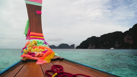 wooden longtail boat with floral garlands hang off of front as it floats in southeast asia waters