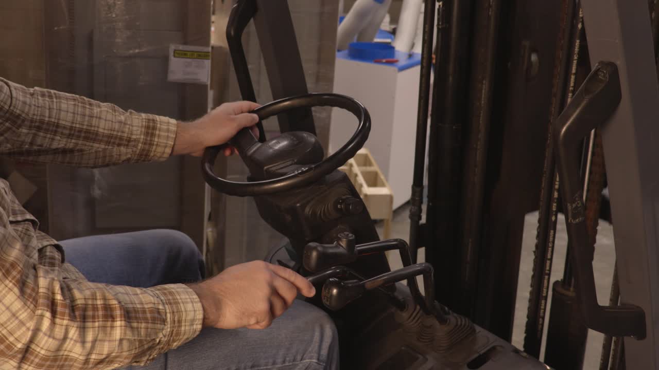 Side View of a Blue Collar Worker Operating an Electric Fork Lift's Levers.