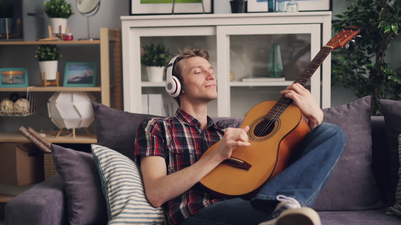 Homem Tocando Violão no Sofá com Fones de Ouvido