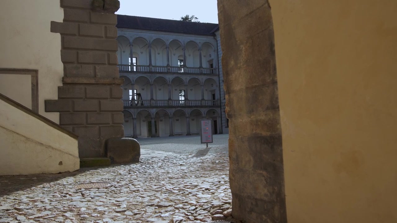 Telecamera a mano che si muove attraverso un cancello di pietra nel cortile del Castello di Jindřichův Hradec, Repubblica Ceca, con portici.
