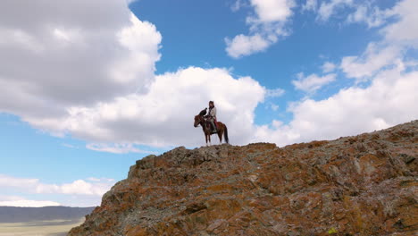 Eagle-Hunter-Riding-A-Horse-On-Top-Of-The-Cliff-In-Western-Mongolia---Drone-Shot