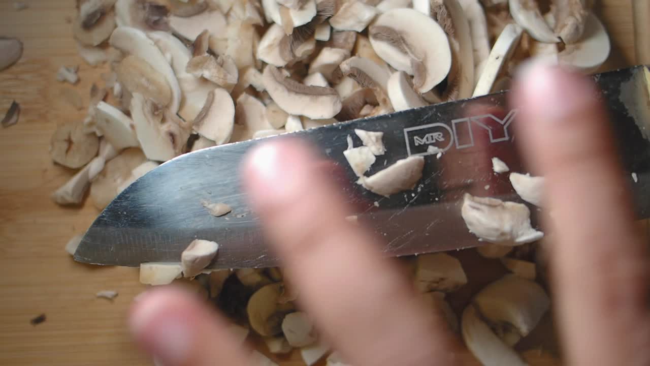 Primo piano di una mano che affetta funghi freschi su un tagliere di legno