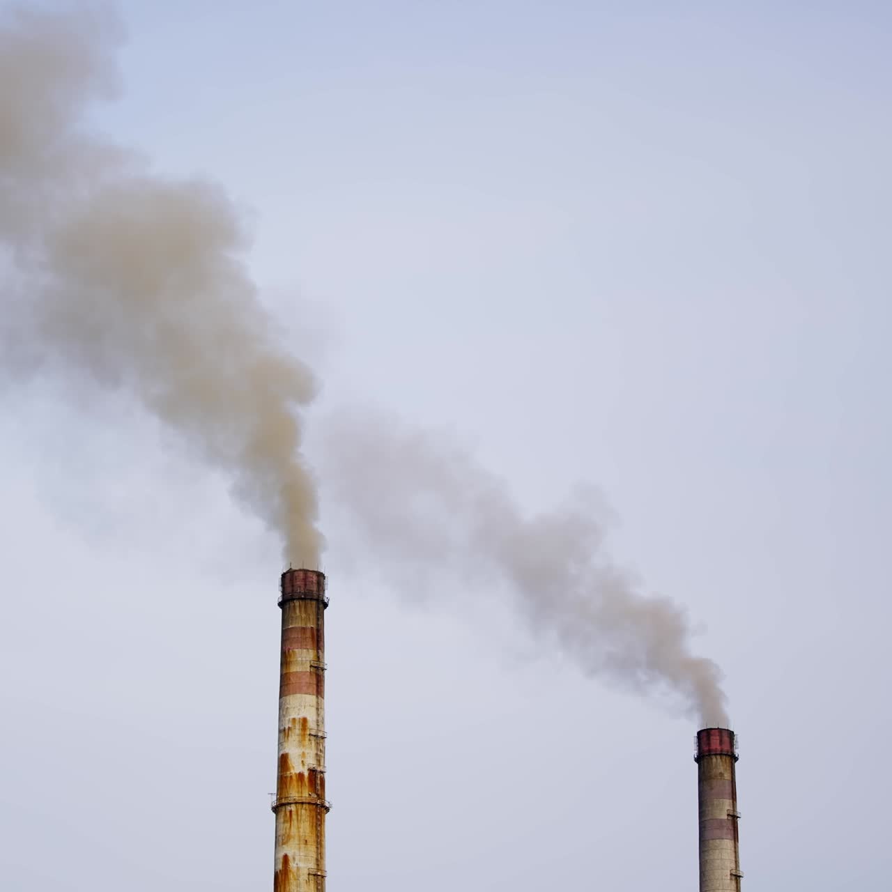 High chimneys of industrial plants smoke against sky background. Dirty factory chimneys are blowing huge puffs of smoke into air. Environmental poisoning by chemical industry