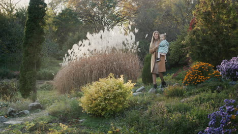 mom with her daughter in her arms walks in a picturesque autumn park. walks along the path along the flowers and reeds