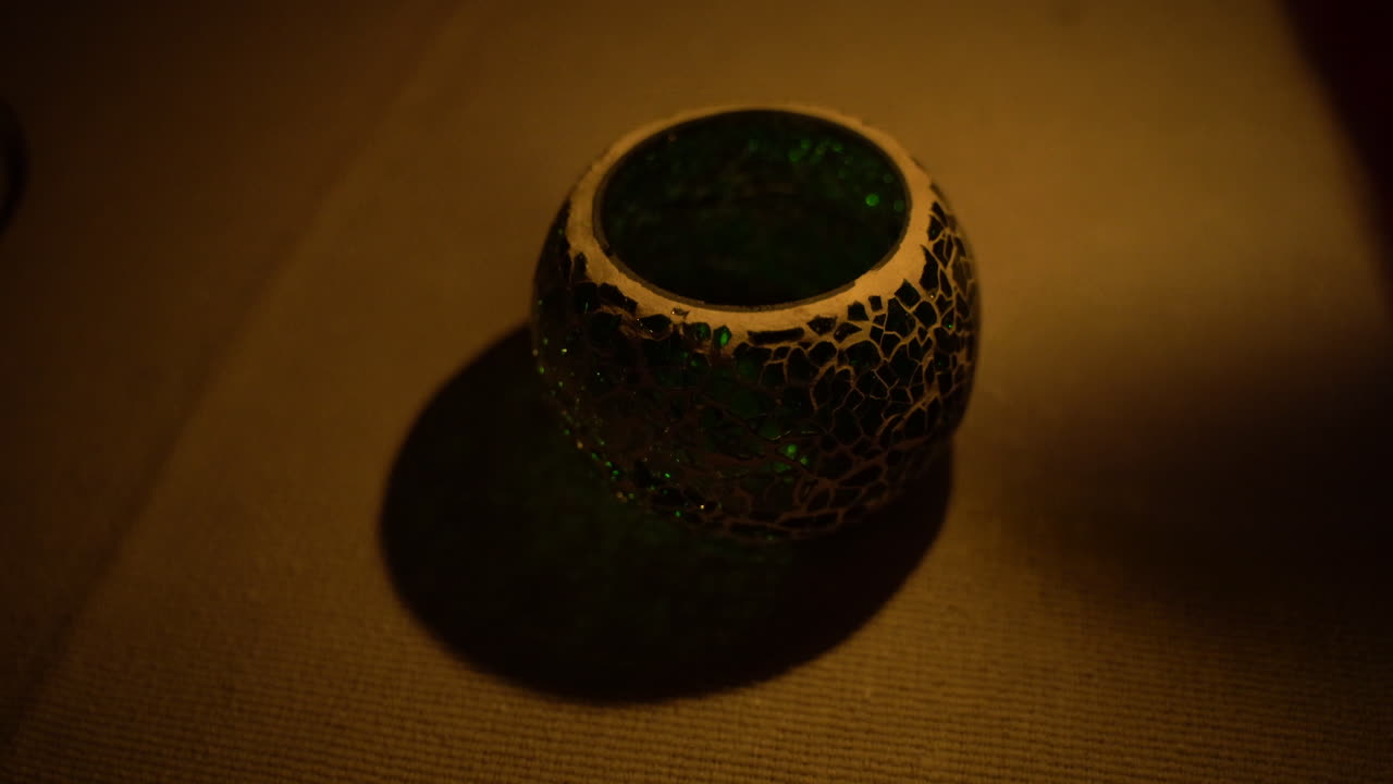 top view of a hand lighting a decorative crystal candle on fire with another wax candle in a dark rorom