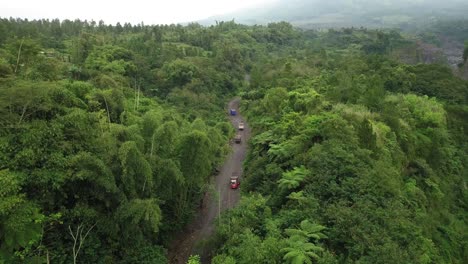 Toma-Aérea-De-Pájaros-De-Camiones-Que-Circulan-Por-Caminos-Rurales-Entre-Bosques-En-La-Ladera-Del-Volcán-Merapi---Transporte-Para-Mina-De-Arena-En-Indonesia---Tiro-Ascendente