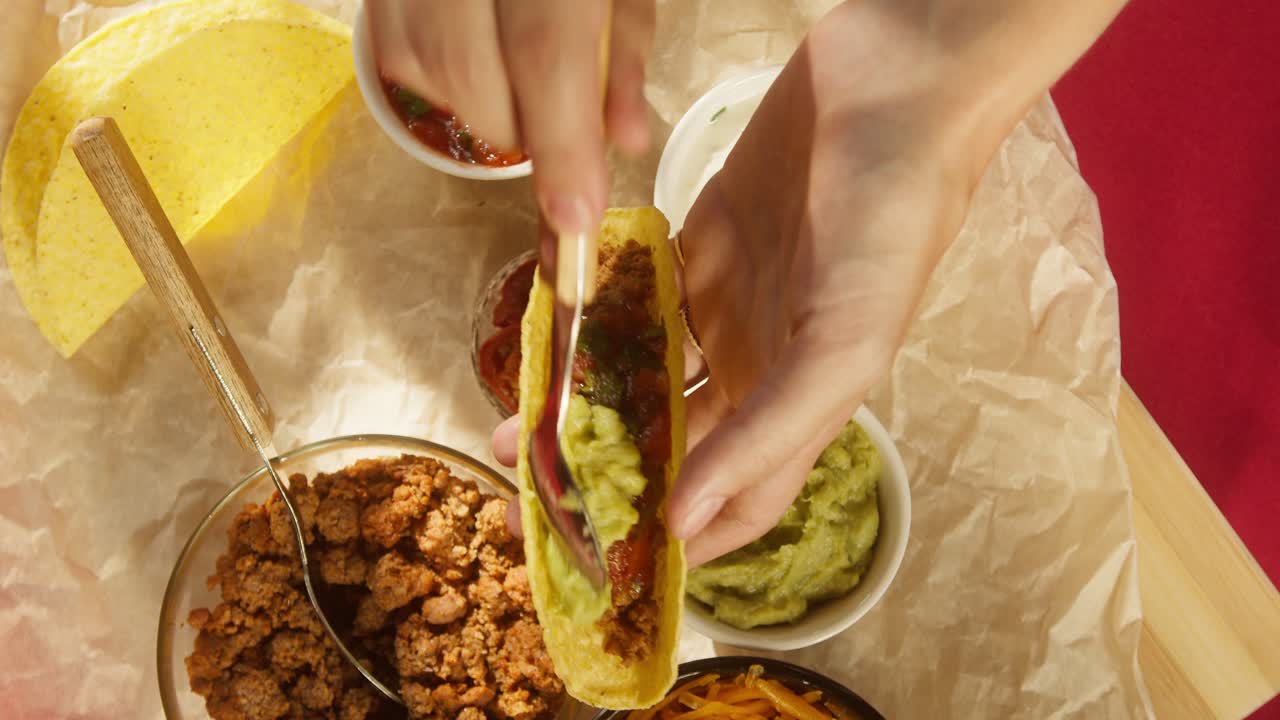 Nærbillede af hånd, der fylder en lækker taco med friske ingredienser.