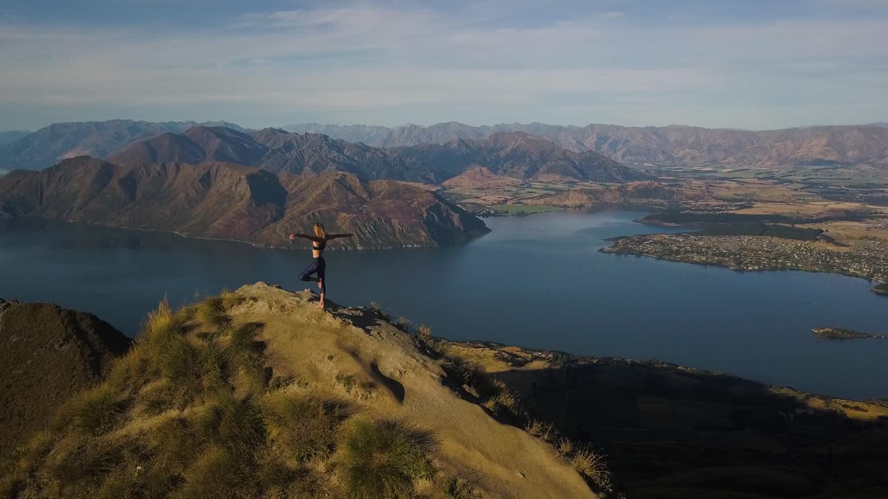 키 큰 금발의 여자가 뉴질랜드 산 정상에서 요가를 하고 있다
