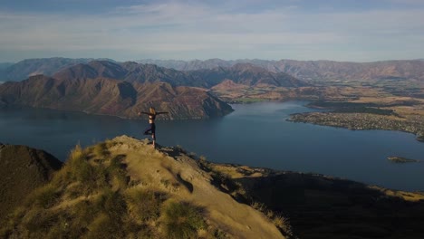 una mujer alta y rubia está haciendo yoga en la cima de una montaña en nueva zelanda