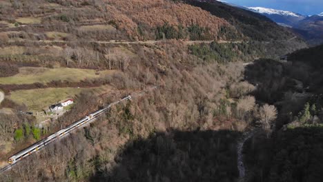 aerial: passenger train going through a valley in a mountainous landscape and snow covered peaks in the background