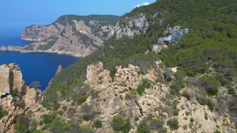 group of tourists hiking on a rocky cliff in ibiza, spain, enjoying the breathtaking view of the mediterranean sea. lovely aerial view flight circle drone footage