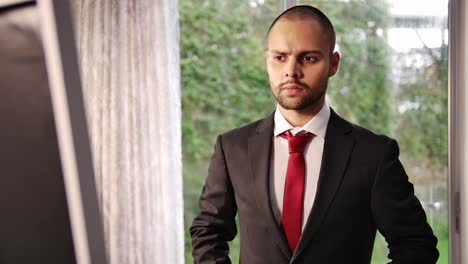 bald young man getting ready and putting on his tie in front of a mirror before job interview at home