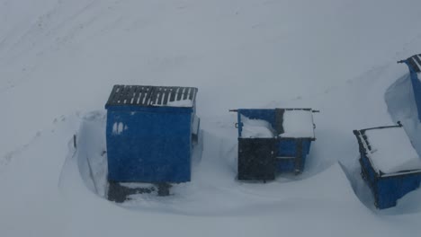 three blue garbage containers abandoned under heavy snow fall