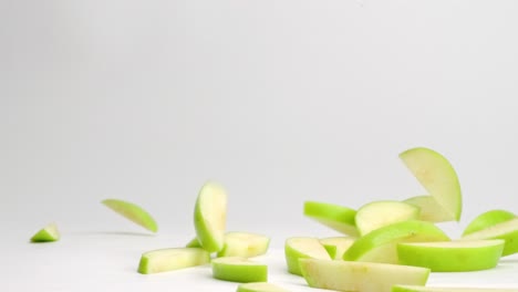 sliced green granny smith apple pieces falling and bouncing on white table top in slow motion