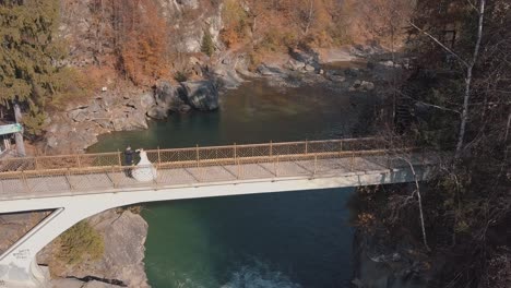 Frischvermählte.-Braut-Und-Bräutigam-Auf-Einer-Brücke-über-Einem-Gebirgsfluss.-Luftaufnahme