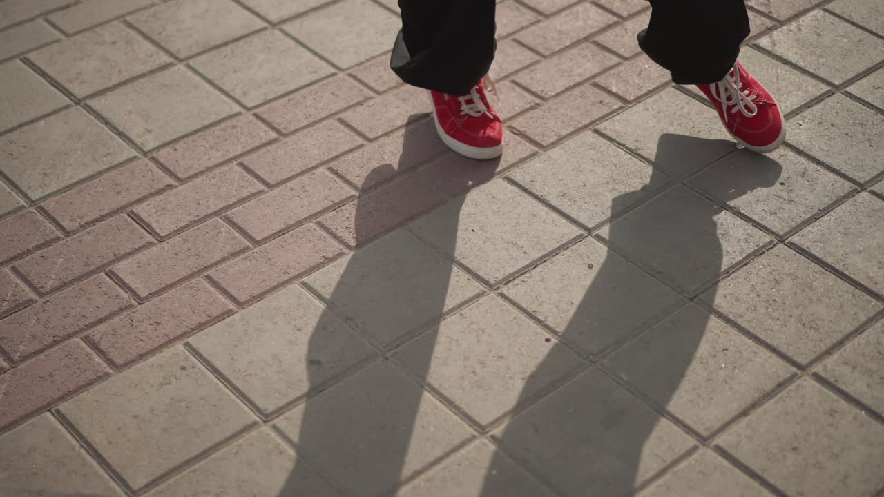 street pavement closeup red sneakers tapping, rhythmic footwork captured on sunlit sidewalk tiles. Series shows dancer practicing precise steps, street performer rehearsing grooves, casual walker