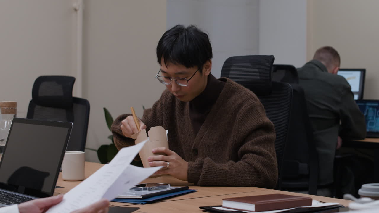Asian man eating noodles at his desk