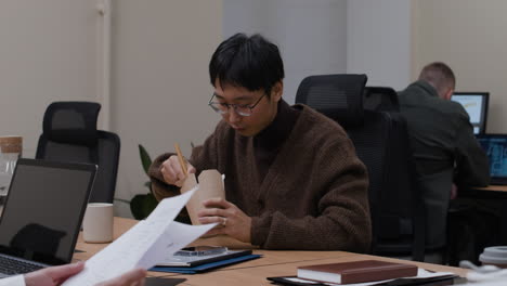 asian man eating noodles at his desk