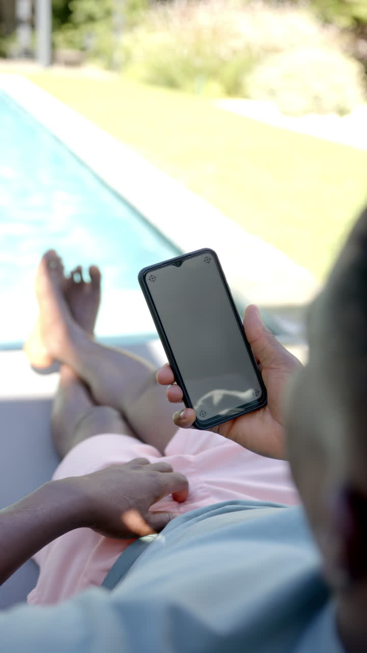 Vertical video: Relaxing by pool, person holding smartphone and lounging on chair