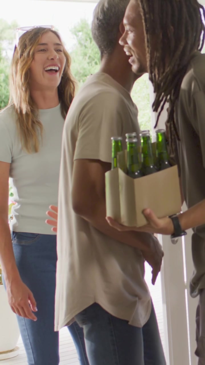 Video verticale: Tre amici in maglietta che arrivano e si salutano sul portico, consegnando un six-pack e una rosa da condividere.