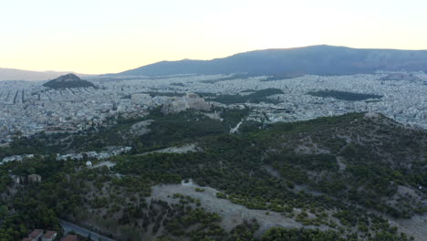 Gran-Toma-Aérea-De-Drones-De-La-Ciudad-De-Atenas-Y-Un-Parque-Verde-Con-La-Acrópolis-Y-La-Ciudad-Central-A-La-Vista,-Grecia