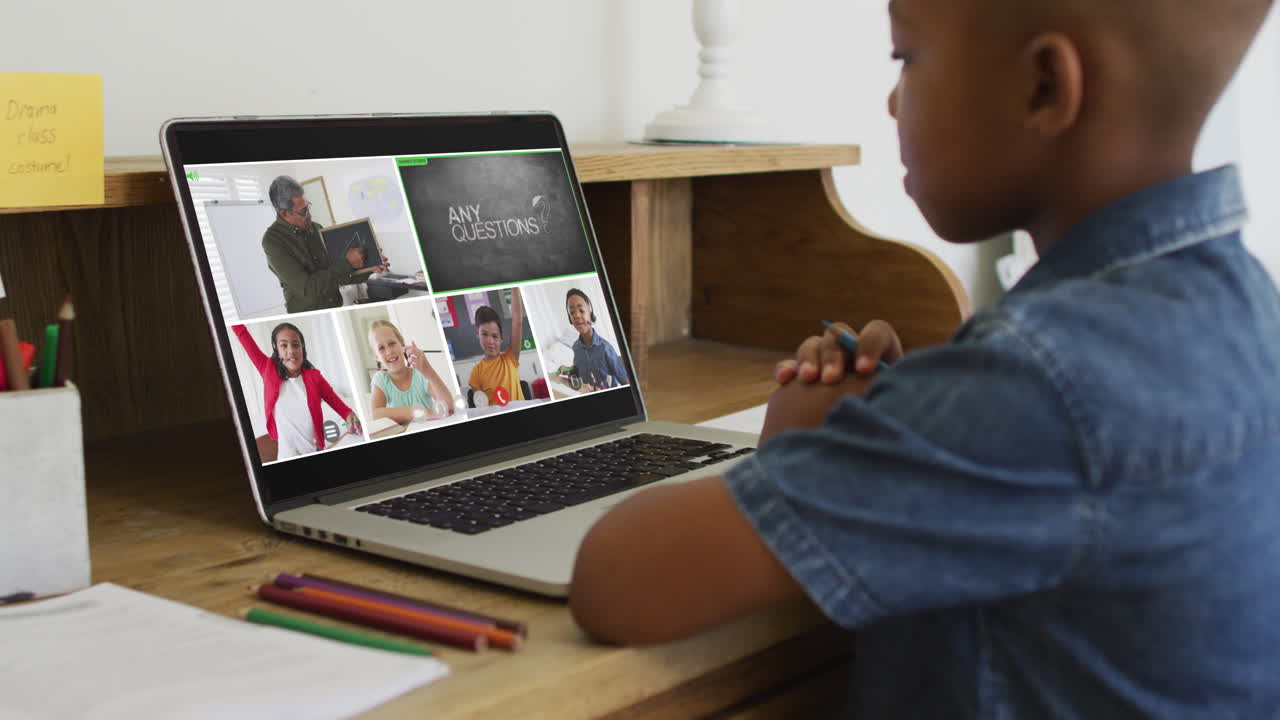 Schoolboy using laptop for online lesson at home, with diverse teacher and class on screen