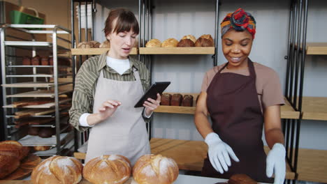 two multiethnic women using tablet and working in bakery