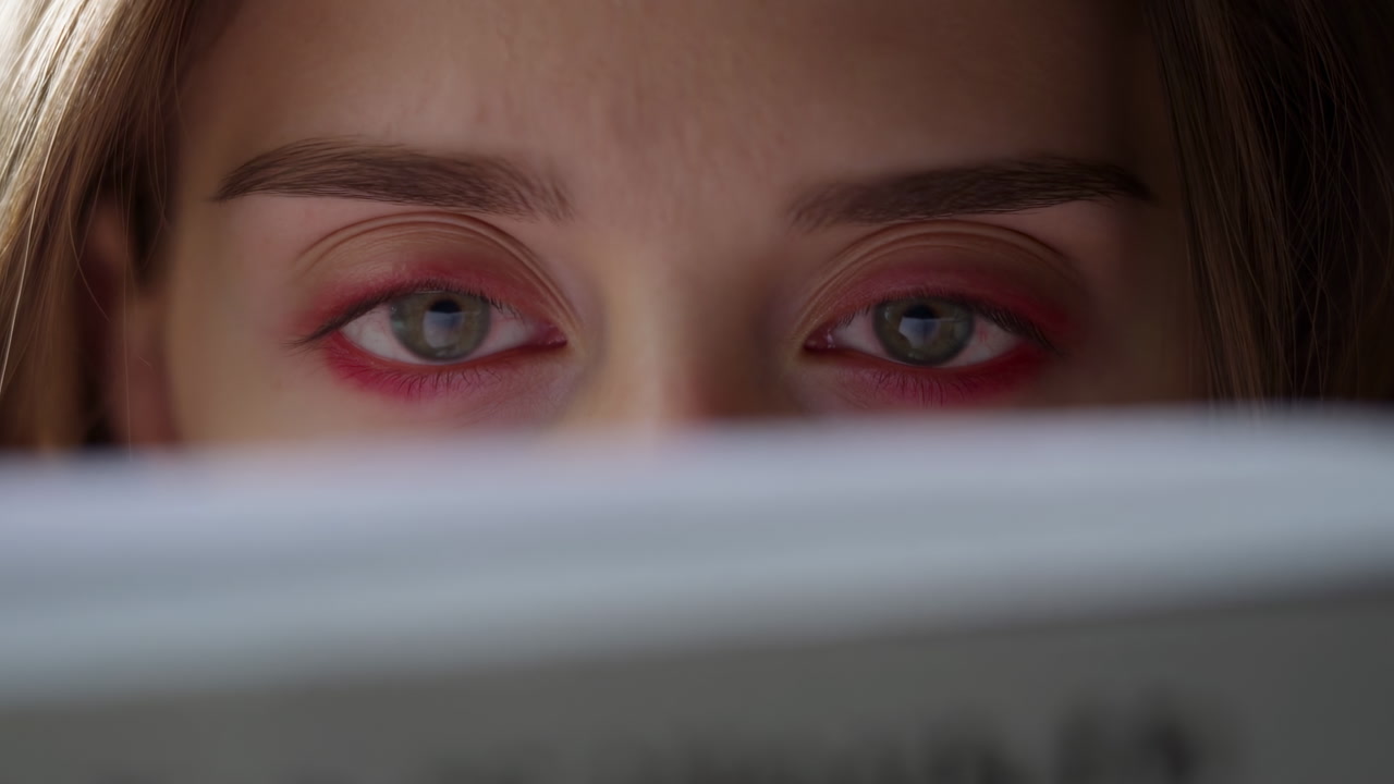 Close Up Caucasian Woman Reading Newspaper, Red Eyeshadow Rim, Pensive Gaze Over Headlines, Soft Natural