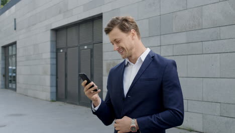 Businessman-using-smartphone-at-street.Entrepreneur-celebrating-victory-outdoors