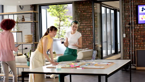 collaborating in modern office, women discussing ideas with laptop and coffee cup